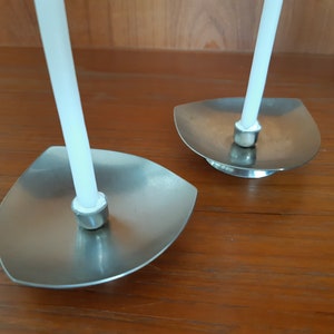 May include: Two silver candle holders with white candles. The holders are shaped like a leaf and have a small round base.