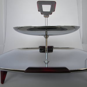 May include: Two-tier serving tray with a chrome finish and red plastic handles. The top tier is round and the bottom tier is square.