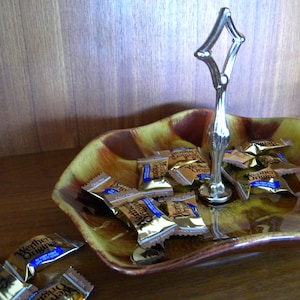 May include: A brown and yellow ceramic candy dish with a silver handle. The dish is filled with individually wrapped Werther's Original sweets.