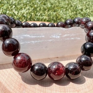 May include: A garnet gemstone bracelet with dark red beads. The bracelet is made of natural stones and is strung on elastic.