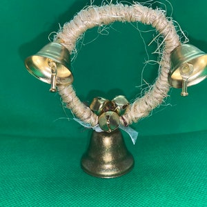 May include: A gold-colored metal bell wreath with a natural twine base. The wreath has three large bells and several smaller bells.