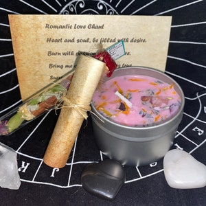 Può includere: Una candela rosa con fiori e erbe secche in una lattina d'argento, un rotolo di pergamena con spago, un tubo di vetro con erbe e fiori secchi, un cristallo bianco, una pietra nera a forma di cuore e una pietra bianca a forma di cuore su uno sfondo nero con un motivo a griglia bianca. La pergamena ha il testo "Romantic Love Chant" e "Heart and soul, be filled with desire. Burn with passion. Bring me c. Suter is true."