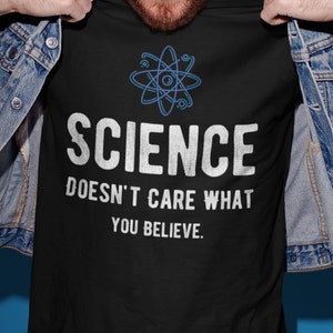 Könnte beinhalten: Ein schwarzes T-Shirt mit einer weißen Atomgrafik und dem Text "SCIENCE DOESN'T CARE WHAT YOU BELIEVE."