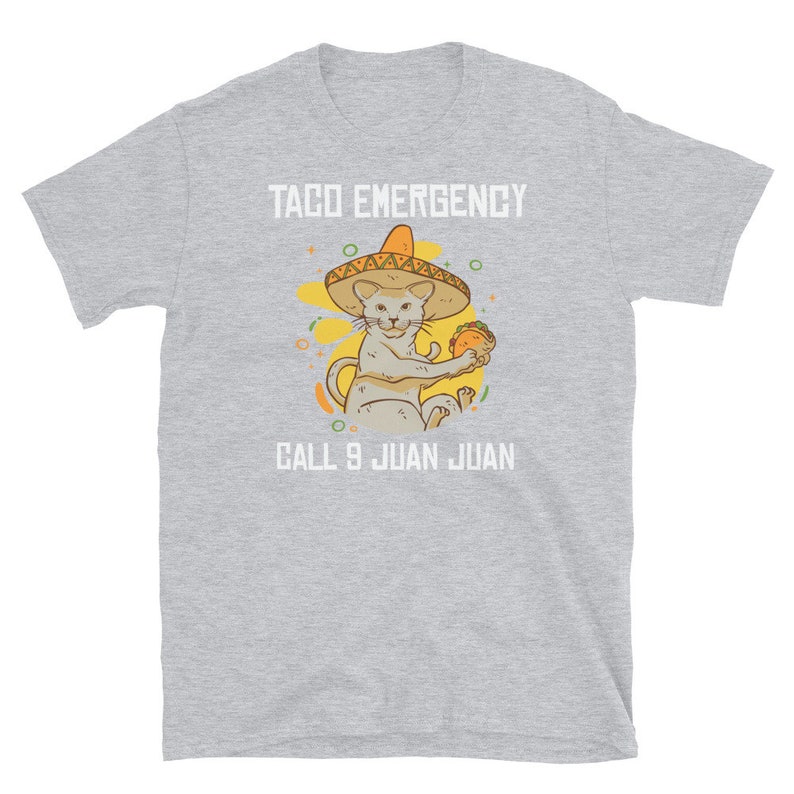 Pode incluir: Uma camiseta cinza com um gr&aacute;fico branco de um gato usando um sombrero e segurando um taco. O texto "Taco Emergency Call 9 Juan Juan" est&aacute; impresso na camiseta.