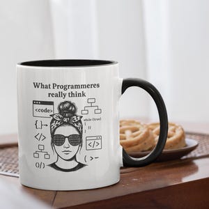Könnte beinhalten: Weißer Keramikbecher mit schwarzem Henkel und Rand. Der Becher zeigt den Text "What Programmeres really think" und eine Grafik einer Frau mit Sonnenbrille und Bandana, umgeben von Codesymbolen.