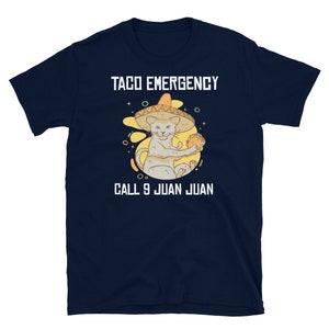 Pode incluir: Uma camiseta azul marinho com um gr&aacute;fico branco de um gato usando um sombrero e segurando um taco. O texto "Taco Emergency Call 9 Juan Juan" est&aacute; impresso na camiseta.
