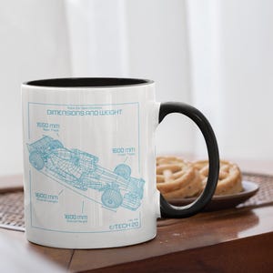 Puede incluir: Taza de cerámica blanca con interior y asa negros. La taza presenta un plano azul de un coche de carreras con especificaciones de dimensiones y peso. Las medidas están en milímetros. El texto de la taza dice "DIMENSIONS AND WEIGHT" y "E/TECH 20".