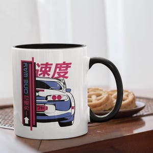 Może przedstawiać: Biały ceramiczny kubek z czarnym wnętrzem i uchwytem. Kubek przedstawia grafikę niebiesko-białego samochodu sportowego z japońskim tekstem. Tekst zawiera słowa "ONE WAY" i "SPEED".