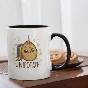 May include: White ceramic mug with a black interior and handle. The mug features a cartoon potato with a unicorn horn and rainbow mane, surrounded by stars, with the word "UNIPOTATE".