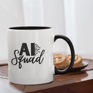 May include: White ceramic mug with a black interior and handle. The mug features the text "AI Squad" in black, with a circuit board graphic. The mug is on a wooden table, with a plate of pastries in the background.