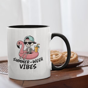 Op de afbeelding: Witte keramische mok met een zwart interieur en handvat. De mok heeft een cartoon skelet met zonnebril en pet, drijvend op een roze flamingo vlot, met een drankje. De tekst "SUMMER-WEEH VIBES" staat op de mok.
