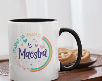 May include: White ceramic mug with a black interior and handle. The mug features the text "Maestra" in a colorful design with a rainbow and hearts. The words "Enseñar es un trabajo de corazón" are also printed on the mug.