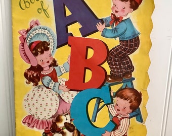 May include: A vintage children's book cover with a yellow background and the title "The Book of ABC". Three children are holding large colorful letters A, B, and C. The book is priced at 15 cents.