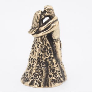 May include: A bronze sculpture of a couple in an embrace, kissing. The woman's dress features a rose pattern. The figures are closely entwined, suggesting a romantic theme. The sculpture is set against a white backdrop.