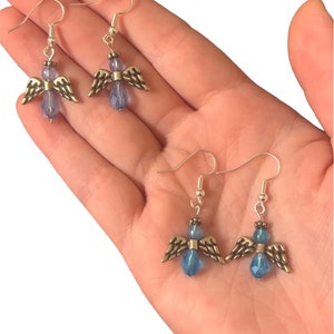 May include: A pair of silver angel dangle earrings with blue crystal beads. The earrings have a hook closure.