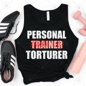 May include: Black tank top with the words "PERSONAL TRAINER TORTURER" in white block letters. The word "TRAINER" is crossed out in red. Black and white athletic shoes, a pink dumbbell, and a pink water bottle are also in the image.