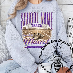 May include: A heather gray sweatshirt with a purple and white graphic. The graphic includes the words "SCHOOL NAME" and "TRACK" above an image of a track and running shoes. Below the image is the word "Mascot".