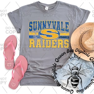 Pode incluir: Camiseta cinza com o texto "SUNNYVALE RAIDERS" em azul e amarelo. Chinelos rosa e um chapéu de palha estão ao lado da camiseta. Uma aplicação de ganga com um gráfico de abelha também é visível.