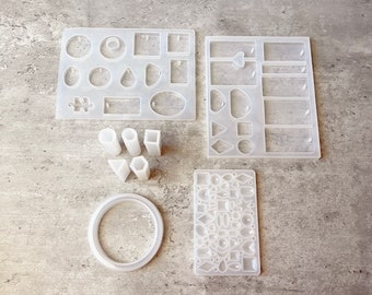 May include: A set of clear silicone molds for making jewelry. The molds include various shapes, such as circles, squares, rectangles, triangles, and ovals. There are also molds for making earrings, pendants, and rings.