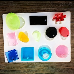 May include: A white silicone mold with 11 different shapes for making resin jewelry. The shapes include a circle, a square, a rectangle, a puzzle piece, a teardrop, a crescent moon, a ring, and a few other abstract shapes.
