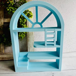 May include: A pale blue wooden shelf unit shaped like a window. It features several shelves, a small staircase, and a ladder. The top section has a semi-circular design with vertical and diagonal beams.