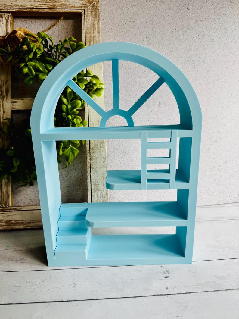 May include: A pale blue wooden shelf unit shaped like a window. It features several shelves, a small staircase, and a ladder. The top section has a semi-circular design with vertical and diagonal beams.