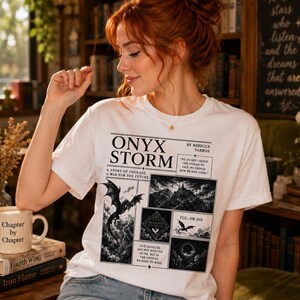 May include: White t-shirt featuring a black and white graphic design with the text "ONYX STORM" and illustrations of dragons and landscapes. The shirt also has the text "Chapter by Chapter" on a mug.