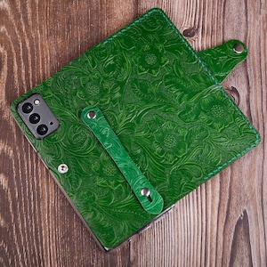 Peut inclure: Étui de téléphone en cuir vert avec un motif en relief floral. L'étui a un rabat avec une fermeture à pression et une sangle pour tenir le téléphone.