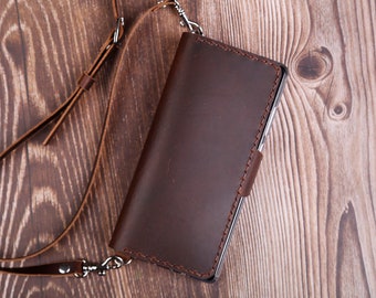 May include: A brown leather phone case with a strap. The case has a stitched edge and a silver clasp.