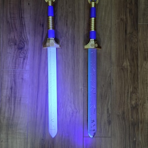 Puede incluir: Dos espadas decorativas con hojas blancas y azules brillantes. Los mangos son dorados, azules y dorados, con una parte superior decorativa. Las espadas se exhiben sobre un fondo de madera.