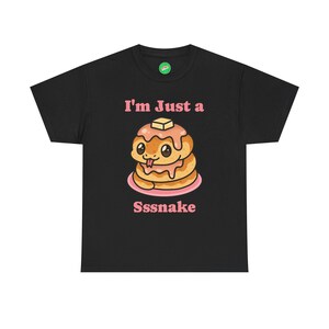 May include: Black t-shirt featuring a cartoon pancake with a snake-like tongue and the text "I'm Just a Sssnake" in pink. The pancake has butter on top and is on a pink plate.
