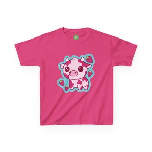 May include: A vibrant pink t-shirt with a cartoon strawberry cow design. The cow is pink with darker pink spots and a light blue outline. Red strawberries are scattered around the cow. The shirt has a round neckline and short sleeves.