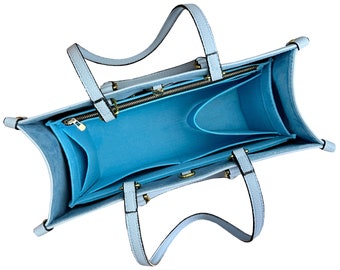 May include: A light blue tote bag with a blue felt interior. The bag has a zippered pocket and two open pockets inside. The bag has two handles.