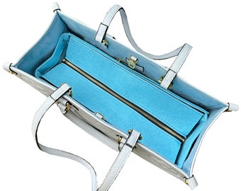 May include: A white leather tote bag with a light blue zippered lining. The bag has two top handles and a zipper closure.