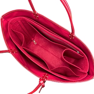 May include: A bright red tote bag featuring a matching red felt organizer insert. The interior organizer includes multiple open compartments, a zippered pocket, and a small metal clasp, providing structured storage within the main bag.