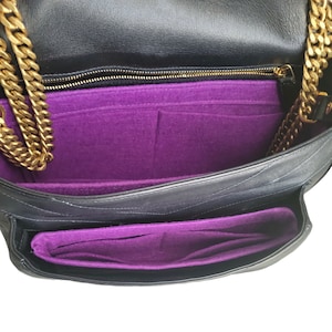 May include: Black quilted leather handbag with a gold chain strap. The interior features a vibrant purple felt organizer with multiple compartments. The bag is open, showcasing the interior design and construction.