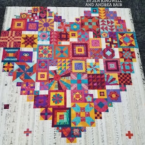 May include: A colorful quilt in the shape of a heart, featuring a patchwork design with various geometric patterns and vibrant colors. The quilt is titled "Boho Heart" by Jen Kingwell and Andrea Bair.