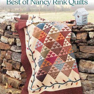 May include: A softcover book titled Best of Nancy Rink Quilts, 9 Classic Quilts from Timeless Blocks, featuring a quilt with a cream background, dark red borders, and a multi-colored triangular block pattern with a vine and leaf border design.