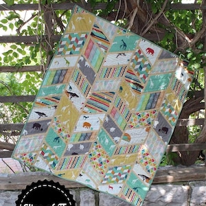 May include: A square quilt featuring a geometric split arrow pattern with various fabric prints including safari animals, colorful triangles, and chevron stripes in shades of yellow, teal, gray, and white. The text "Split Arrows" and "Slice of Pi Quilts" appear.