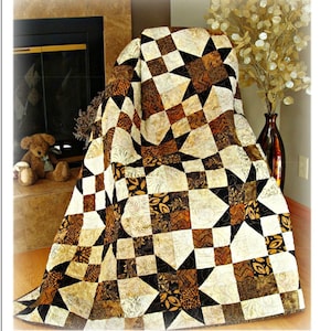 May include: A quilt pattern with a geometric design in shades of brown, black, and cream. The quilt is draped over a chair. The text "Simply Elegant Quilt Pattern" is visible, with size options for Twin (60" x 84"), Queen (84" x 108"), and King (108" x 108").