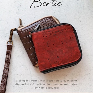 May include: Two compact wallets with zipper closures. One is brown with a crocodile pattern, the other is red with a textured surface. The wallets are labeled "Bertie" and are from Sallie Tomato.