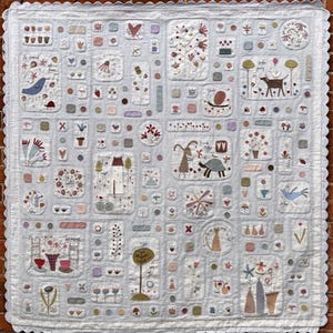 May include: A patchwork quilt with a light blue background and various colorful appliques. The appliques include flowers, animals, houses, and other whimsical designs. The quilt is edged with a scalloped border.