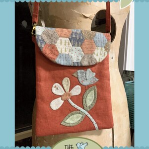 May include: Red satchel with a flap featuring a patchwork design. The satchel has a floral and bird applique. The text "My Red Satchel" is at the top, and "The Birdhouse Patchwork Designs" is at the bottom.
