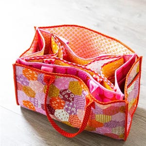 May include: A patchwork fabric tote bag with a red handle and multiple compartments. The bag is made of pink, orange, and purple fabric with a floral pattern.