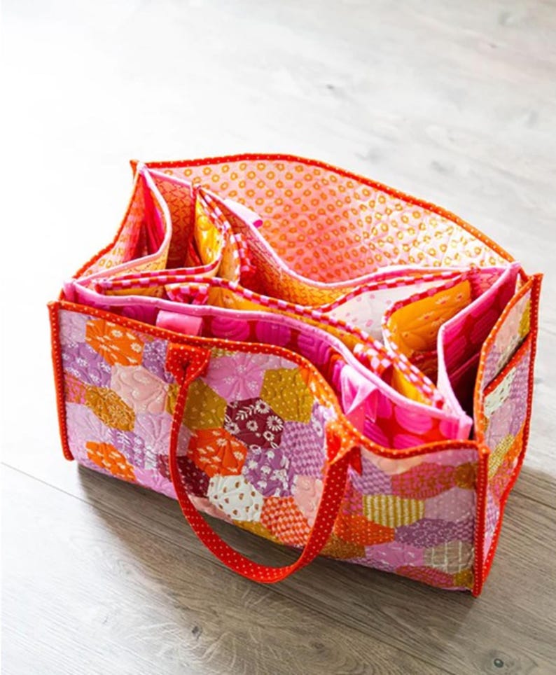 May include: A patchwork fabric tote bag with a red handle and multiple compartments. The bag is made of pink, orange, and purple fabric with a floral pattern.
