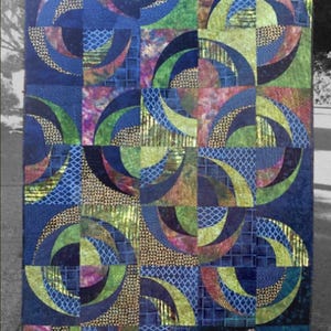 May include: A quilt pattern called "Blue Onion" with a geometric design featuring blue, green, and gold circles and squares. The quilt is made by Saginaw St Quilts and has the pattern number P452.
