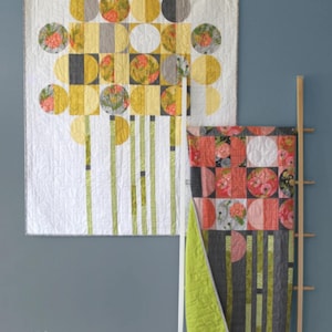 May include: Two handmade quilts with a floral and geometric design. The larger quilt features yellow, gray, and white circles and squares. The smaller quilt has a red, gray, and white floral pattern. The quilts are displayed on a wooden ladder.