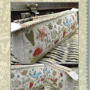 May include: A rectangular pencil case with a beige linen fabric. The case is decorated with embroidered birds, flowers, hearts, and the text "The Little Things". The pencil case has a zipper closure and is displayed on a woven surface.