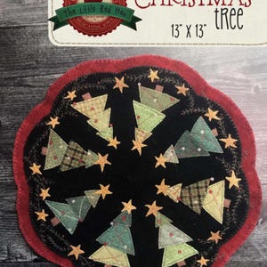 May include: A round, black Christmas tree placemat with a red scalloped edge. The design features appliqued Christmas trees in various green and tan fabrics, surrounded by gold stars. The text "Oh CHRISTMAS tree" is at the top, with the dimensions 13" x 13".