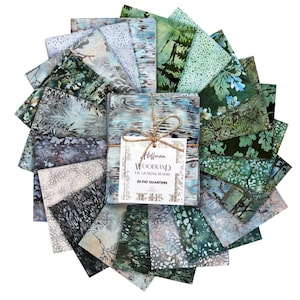 May include: A bundle of 20 fat quarters of fabric in shades of blue, green, and gray, arranged in a circular pattern. The fabric features various nature-inspired designs, including trees and water patterns. The bundle is tied with twine and includes a tag that reads "Hoffman Woodland".